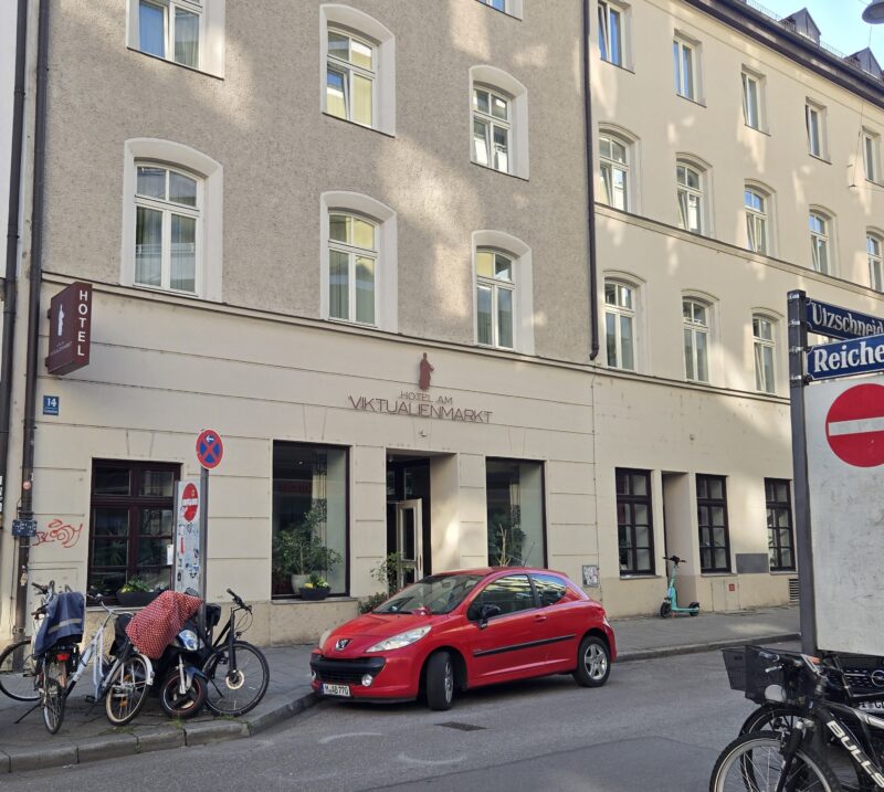 Street scene with a row of beige buildings, bicycles parked along the curb, and a red car in the foreground.