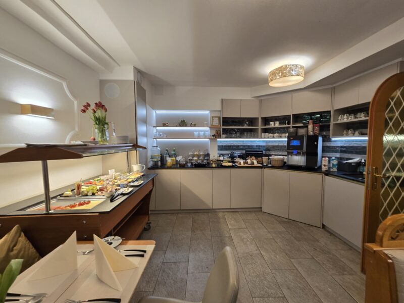 Cafe interior with pastry displays along a curved counter and a vase of red flowers on the front counter, beige cabinetry in the background.