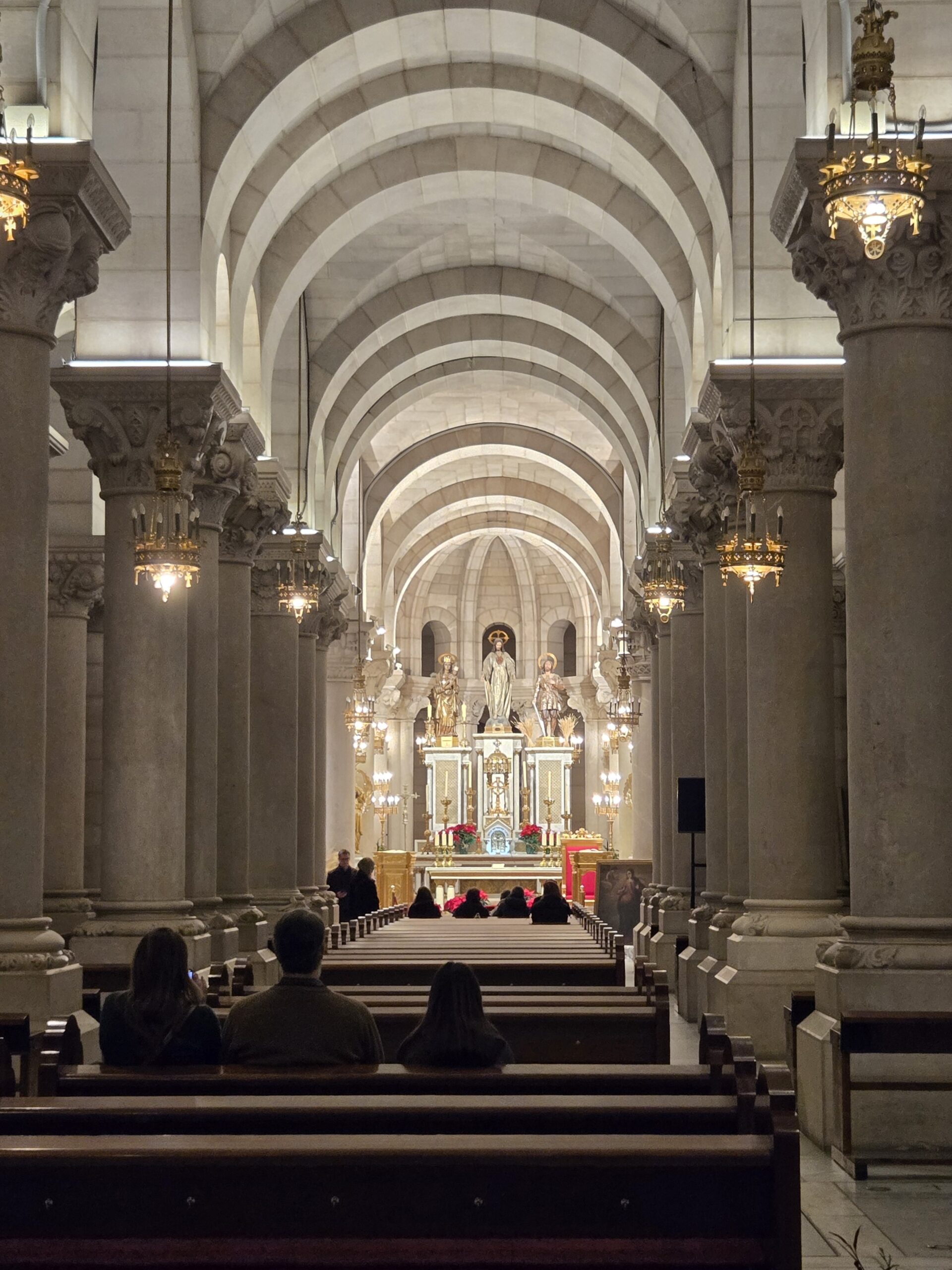 Interior of a grand cathedral with tall arches and rows of pews leading to an ornate altar.