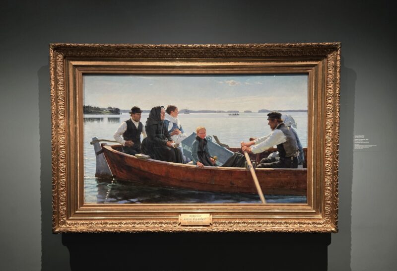 Group of people in a wooden rowboat on a calm lake, with a woman in a black shawl and a child at the bow, by the shore.