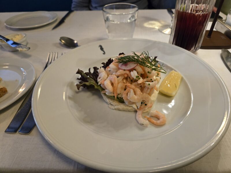 Shrimp crostini appetizer with dill, lemon wedge, and greens on a white plate.