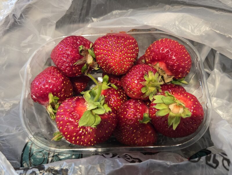 Fresh, ripe strawberries in a clear plastic container on a crinkled metallic surface.
