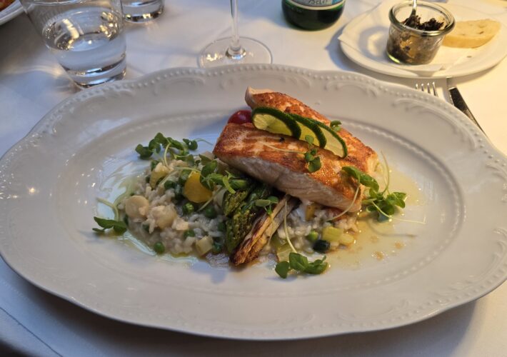 Pan-seared fish fillet on creamy risotto with peas, microgreens, and a lime garnish on a decorative white plate.