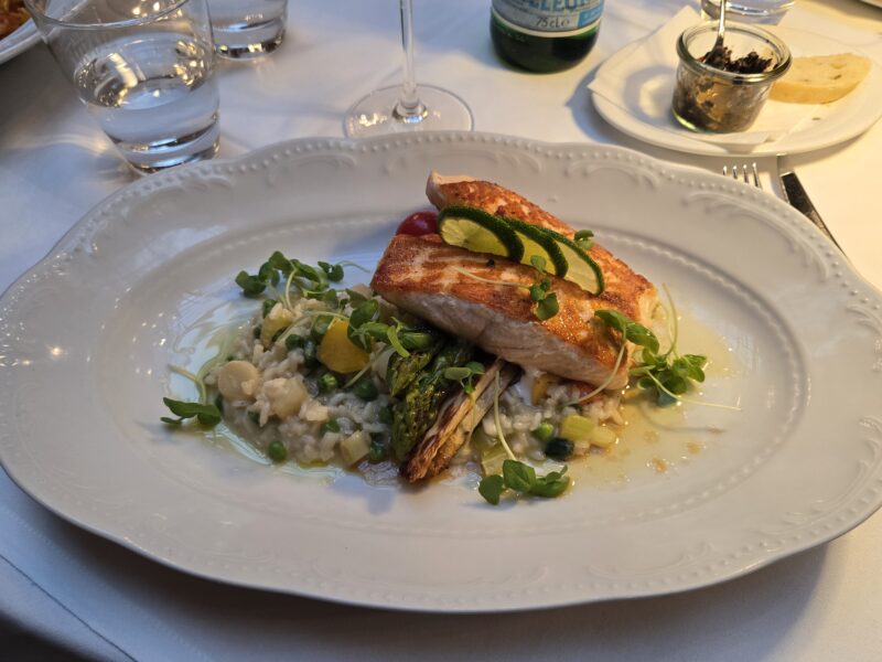 Pan-seared fish fillet on creamy risotto with peas, microgreens, and a lime garnish on a decorative white plate.